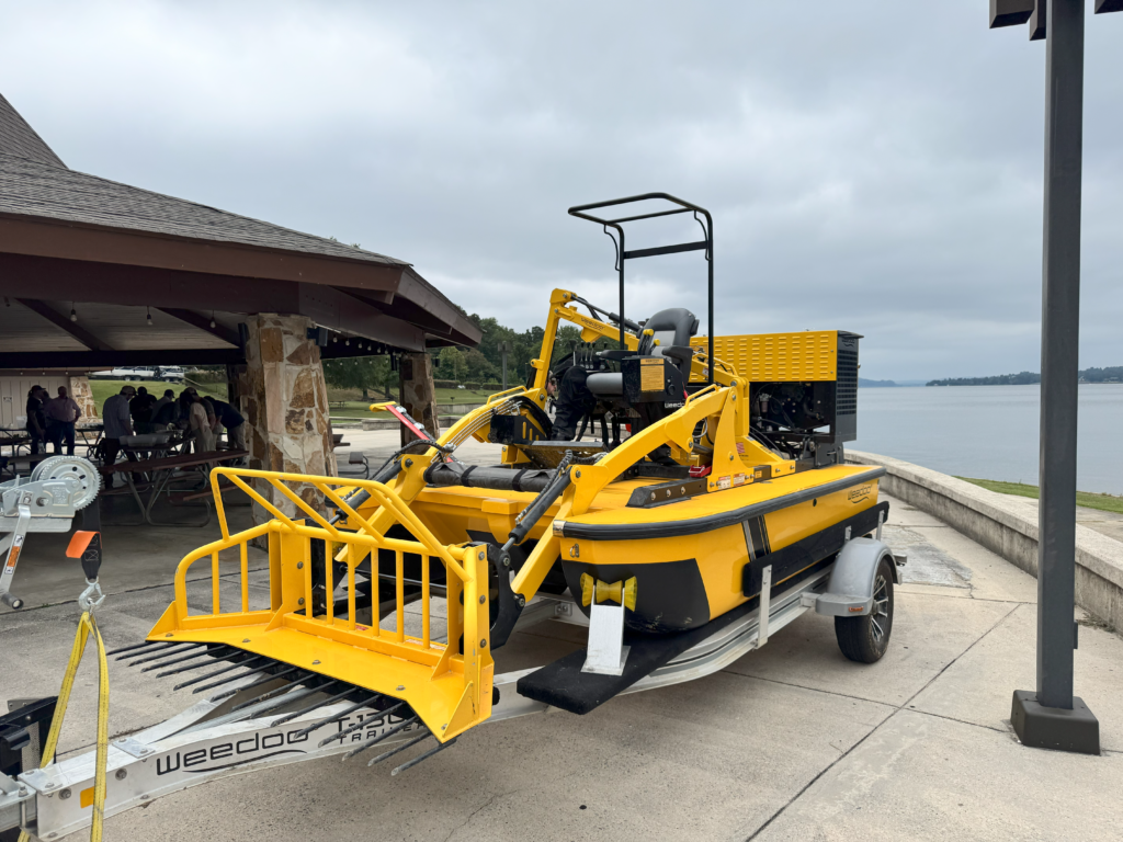 A yellow and black aquatic plant harvesting machine on display outdoors.